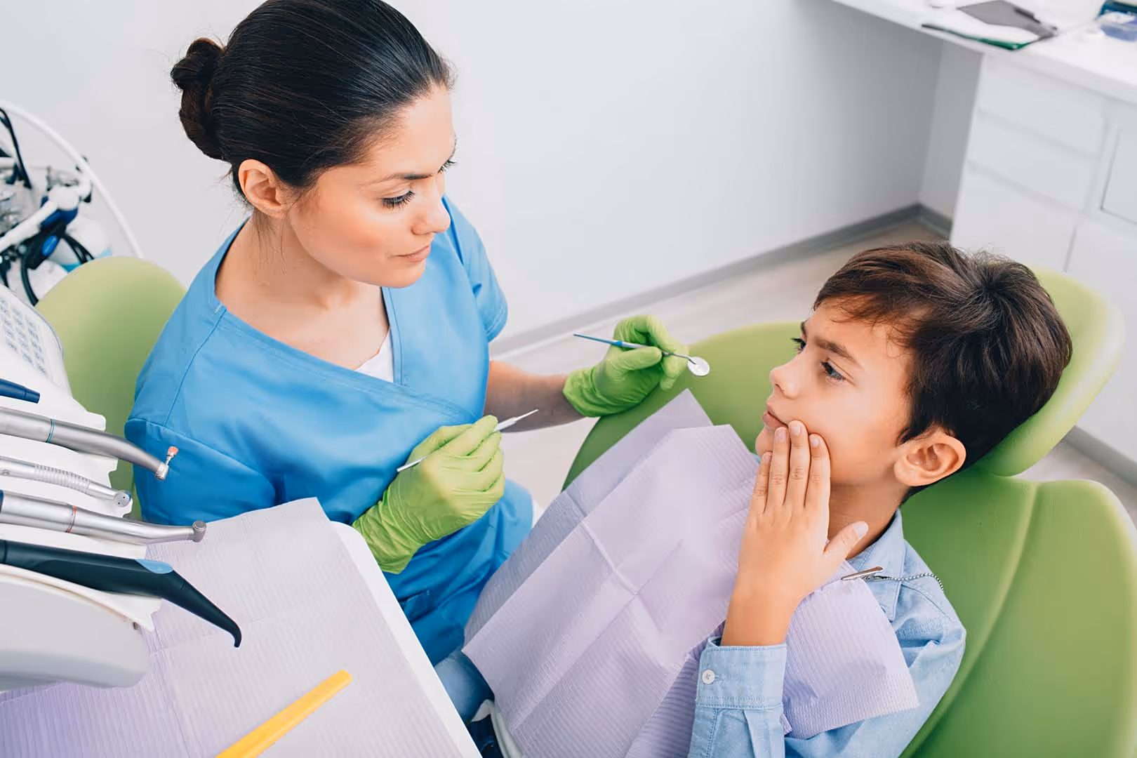 Sadness little boy showing tooth pain to his dentist. He visiting pediatrician dentist