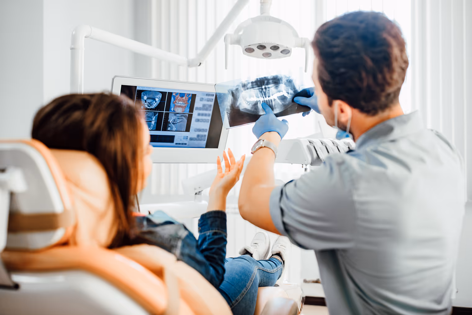 Medicine, dentistry and healthcare concept, male dentist showing teeth x-ray to female patient at dental clinic office.