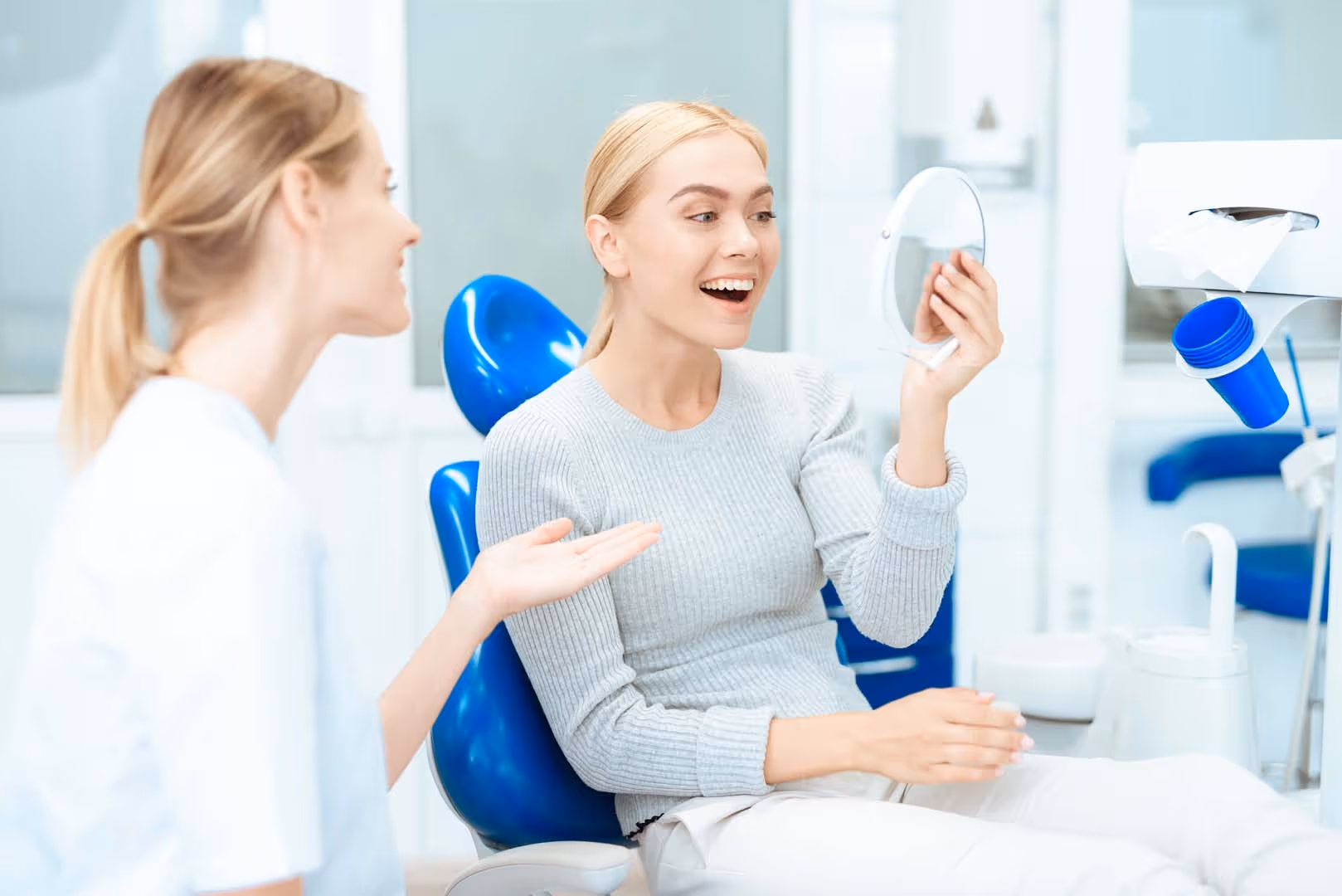 A woman is sitting at a dentist's reception. She looks in the mirror at her teeth. Woman smiling